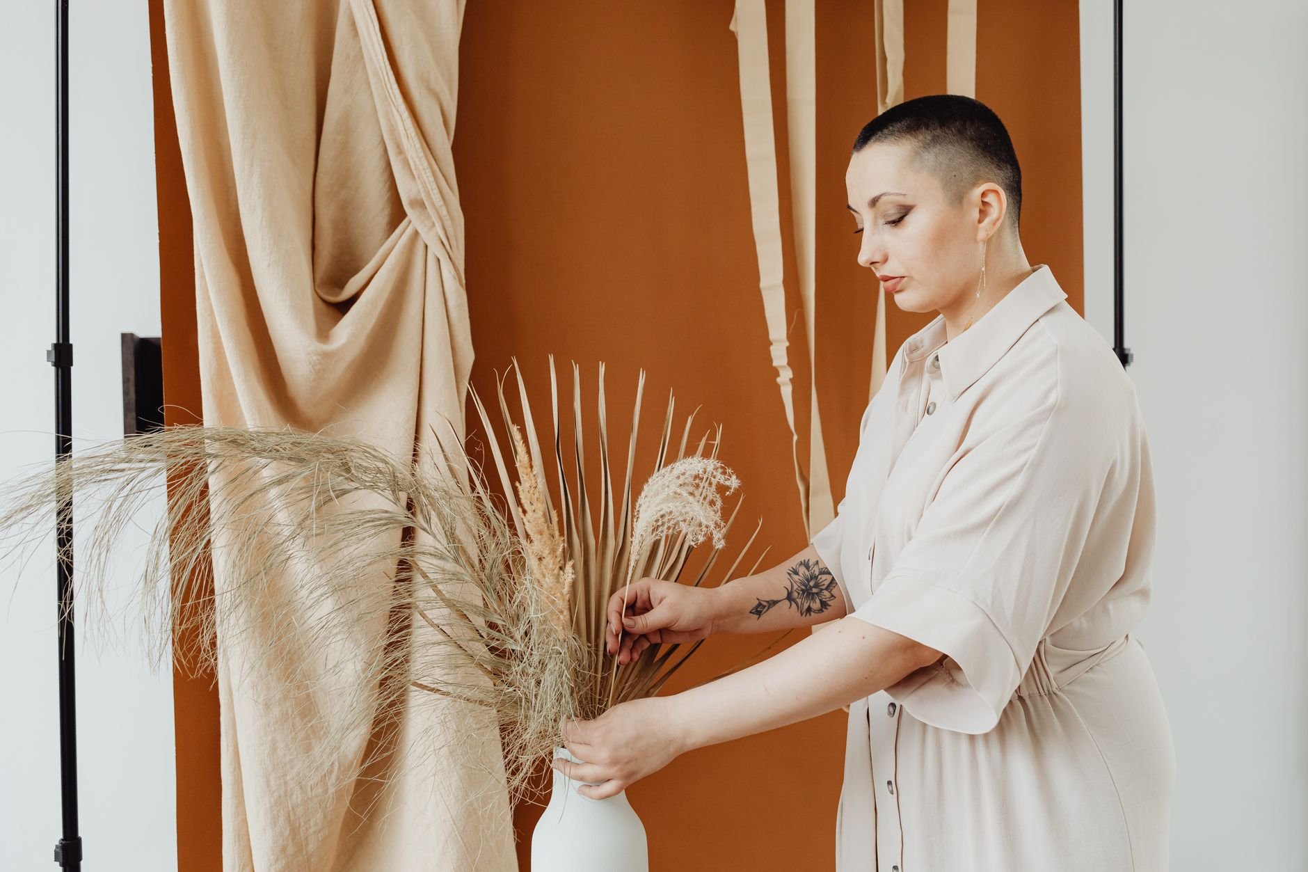 A woman arranging dried flowers in a warm, minimal home interior